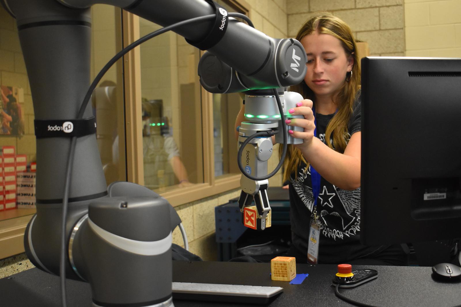 A female student using a mechanical arm to pick up wooden blocks